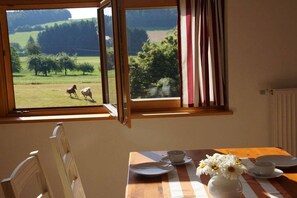 A room with a dining table set for two, a window with curtains, and a view of horses in a field. - Panoramic view of the Höllbach valley (Rettenbach)