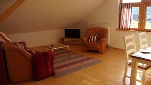 Une pièce confortable de style loft, avec un plafond en bois, un canapé, un fauteuil, une petite table et une fenêtre avec des rideaux.
