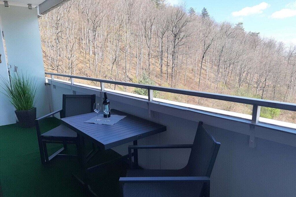 Un balcón con mesa y sillas, con vista a una zona boscosa.