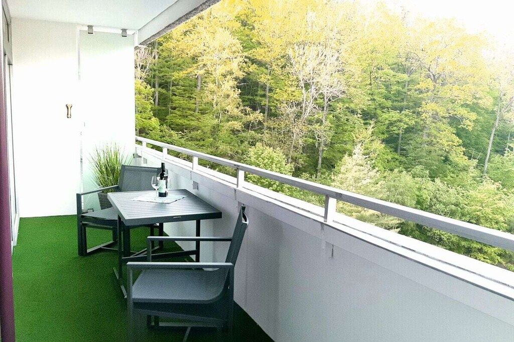 En balkon med et bord og stole, med udsigt over et skovområde.