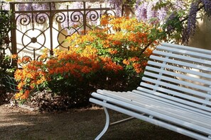 Un banc blanc dans un jardin, agrémenté de fleurs oranges et de glycines violettes.