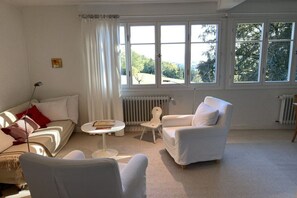 A living room with a sofa, armchair, and a small table. There are large windows with curtains. - 1 Alpenblick - Steineckhof (Schopfheim)