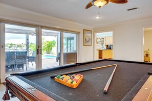 Et billardbord med bolde og kø i et rum med udsigt til en swimmingpool.