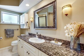 Un bany amb un lavabo de superfície de granit, un mirall gran i un ram de flors seques.