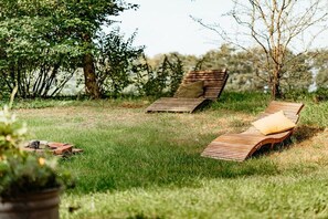 Two wooden lounge chairs in a grassy outdoor area with trees in the background.