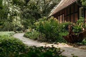A pathway leading to a traditional building with a tiled roof, surrounded by dense greenery and trees.
