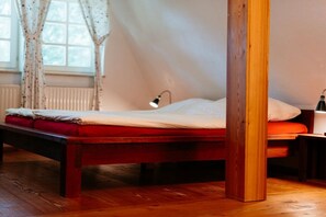 A wooden bed with a red mattress in a room with a window and a lamp.