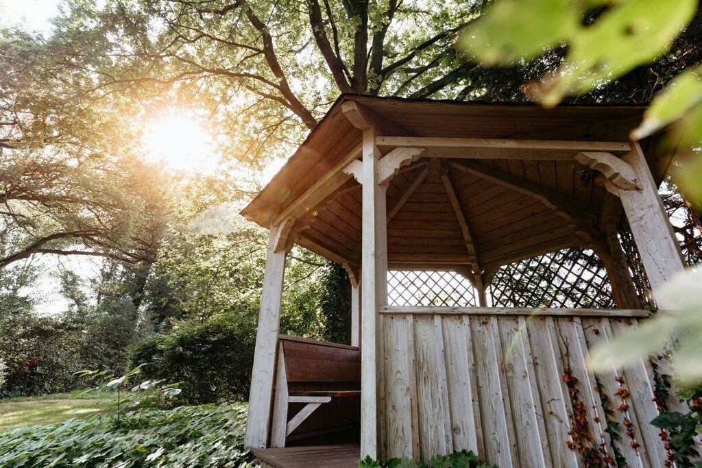 Un kiosque en bois avec un banc, entouré d’arbres et de feuillage.