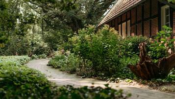 A pathway leading to a traditional building with a tiled roof, surrounded by dense greenery and trees.