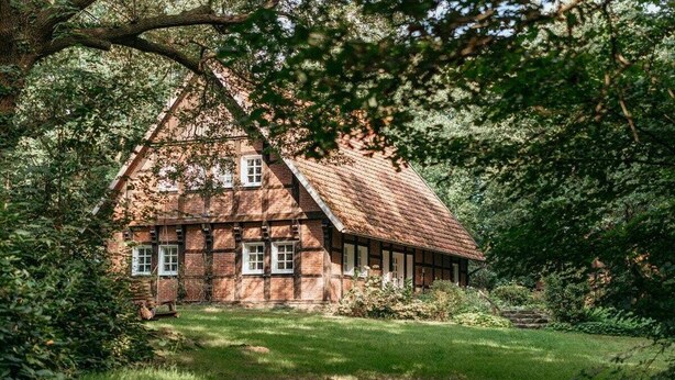 A traditional timber-framed house with a sloped roof, surrounded by lush greenery and a well-maintained lawn.