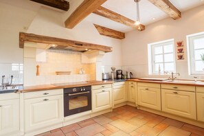 A kitchen with white cabinets, a black oven, wooden beams, and a window with a view.