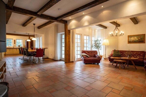 A spacious living area with a wooden floor, a dining table with chairs, a sofa, and a chandelier.