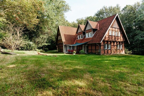 A traditional half-timbered house with a sloped roof, surrounded by a well-maintained lawn and trees.