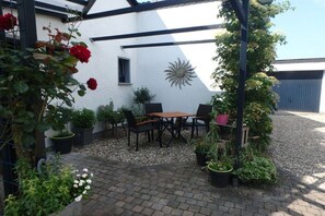 A patio with a table and chairs, surrounded by potted plants and a white wall with a decorative sunburst. - Gingerbread House Xanten (Xanten)