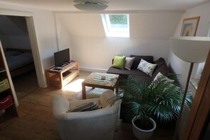 A compact living space with a sofa, armchair, TV, and a potted plant. - Gingerbread House Xanten (Xanten)