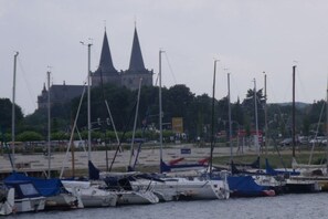 Ein Yachthafen mit vertäuten Booten, eine Kirche mit zwei Türmen im Hintergrund und ein Parkplatz mit Autos.