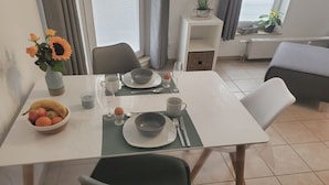 Un comedor con una mesa dispuesta para dos, un cuenco de fruta y un florero con flores.