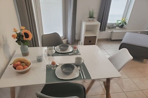 A dining area with a table set for two, a bowl of fruit, and a vase with flowers. - Holiday apartment with 1 bedroom (Bad Kreuznach)