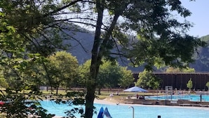 Una piscina con tobogán, rodeada de árboles y con una montaña al fondo.