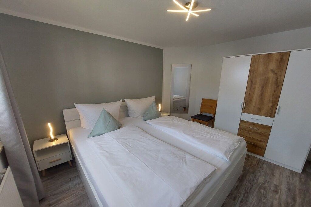 Un dormitorio con una cama grande, mesitas de noche, un armario y un espejo.