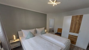 Un dormitorio con una cama grande, mesitas de noche, un armario y un espejo.