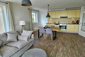 Un salon moderne comprenant un canapé, une table à manger avec des chaises, une cuisine avec des meubles jaunes et une grande fenêtre.