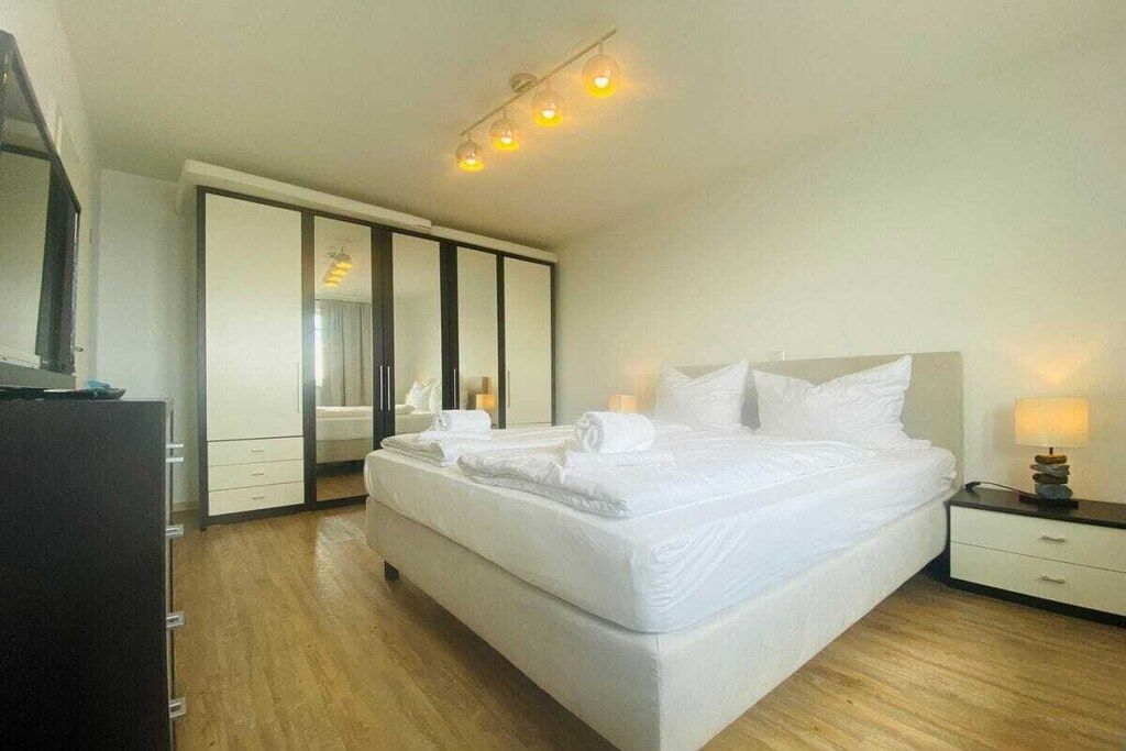 Una habitación de hotel con una cama grande, un armario, una mesita de noche y un espejo.