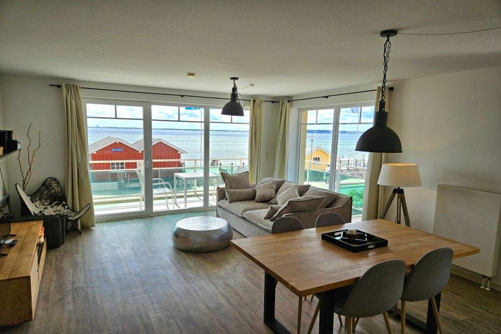 A spacious living area with a wooden table, a sofa, and a view of the sea through large windows.