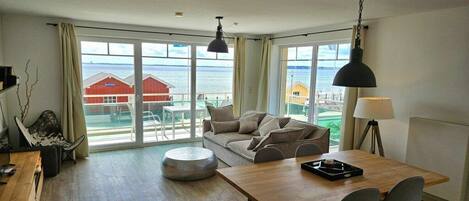 A spacious living area with a wooden table, a sofa, and a view of the sea through large windows.