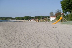 Ein sandiger Strand mit einer gelben Rutsche und einem Rettungsturm im Hintergrund.