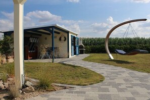 A modern house with a covered porch, a hanging swing, and a paved pathway. - Thatched House Anchorage (Zierow)