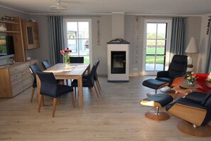 A modern living room with a dining area, a fireplace, and large windows. - Thatched House Anchorage (Zierow)