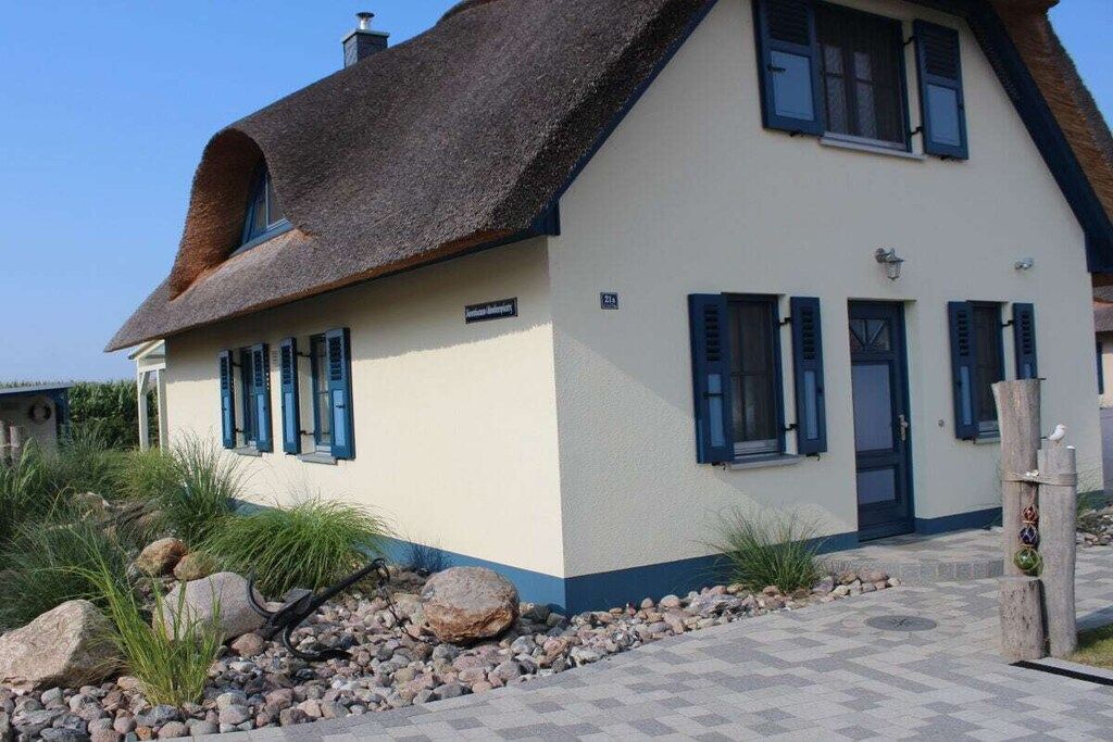 Una casa de dos pisos con techo de paja, fachada blanca y contraventanas azules.