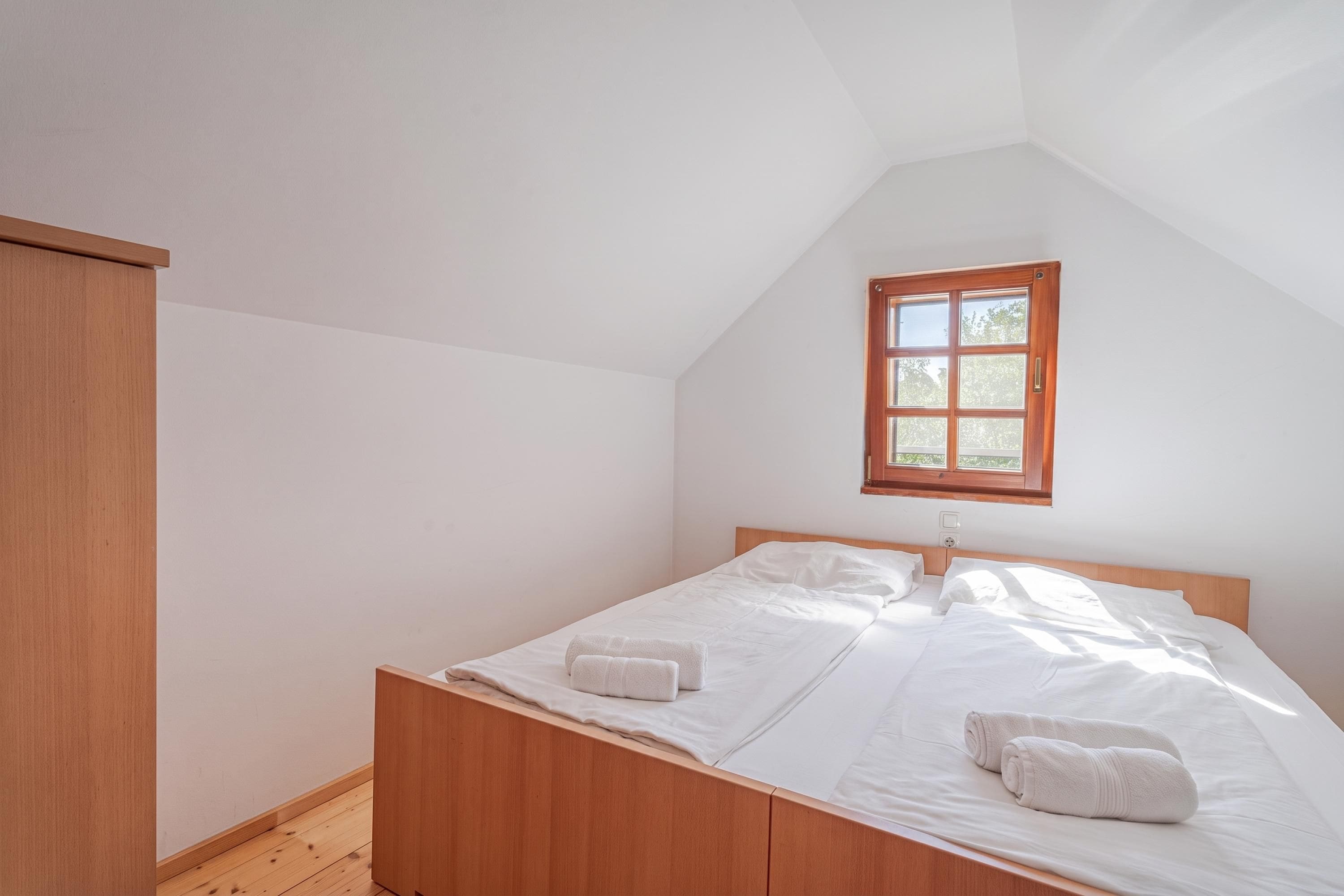 A bedroom with a wooden bed, white linens, and a window with a wooden frame.