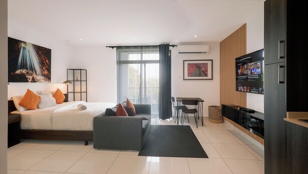 A modern hotel room with a bed, sofa, TV, and a dining area. - Peravi at Embassy Gardens  (Accra)