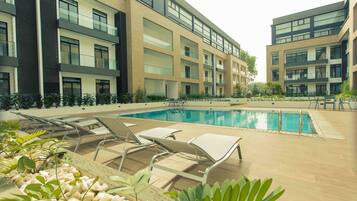 A modern outdoor swimming pool with lounge chairs and a building with multiple balconies in the background.