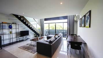 Una sala de estar moderna con un sofá, una mesa de centro y un televisor sobre un mueble. Se ve una escalera que conduce a un balcón con vistas.