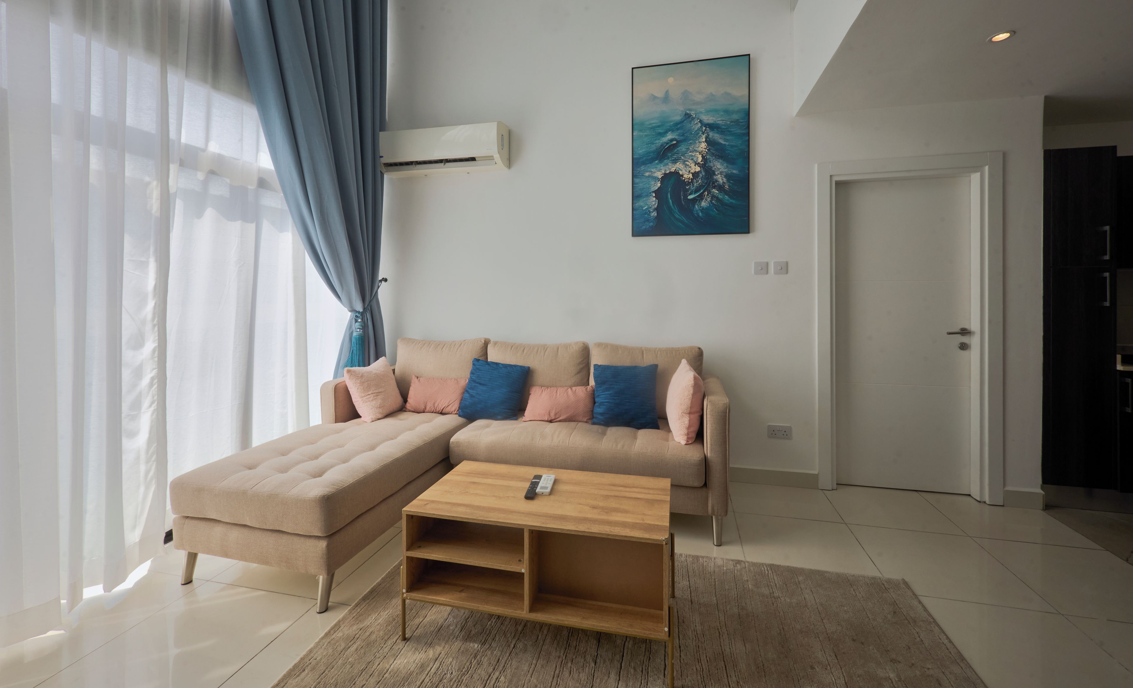 Una sala de estar moderna con un sofá seccional color beige, una mesa de centro de madera y un ventanal con cortinas ligeras.