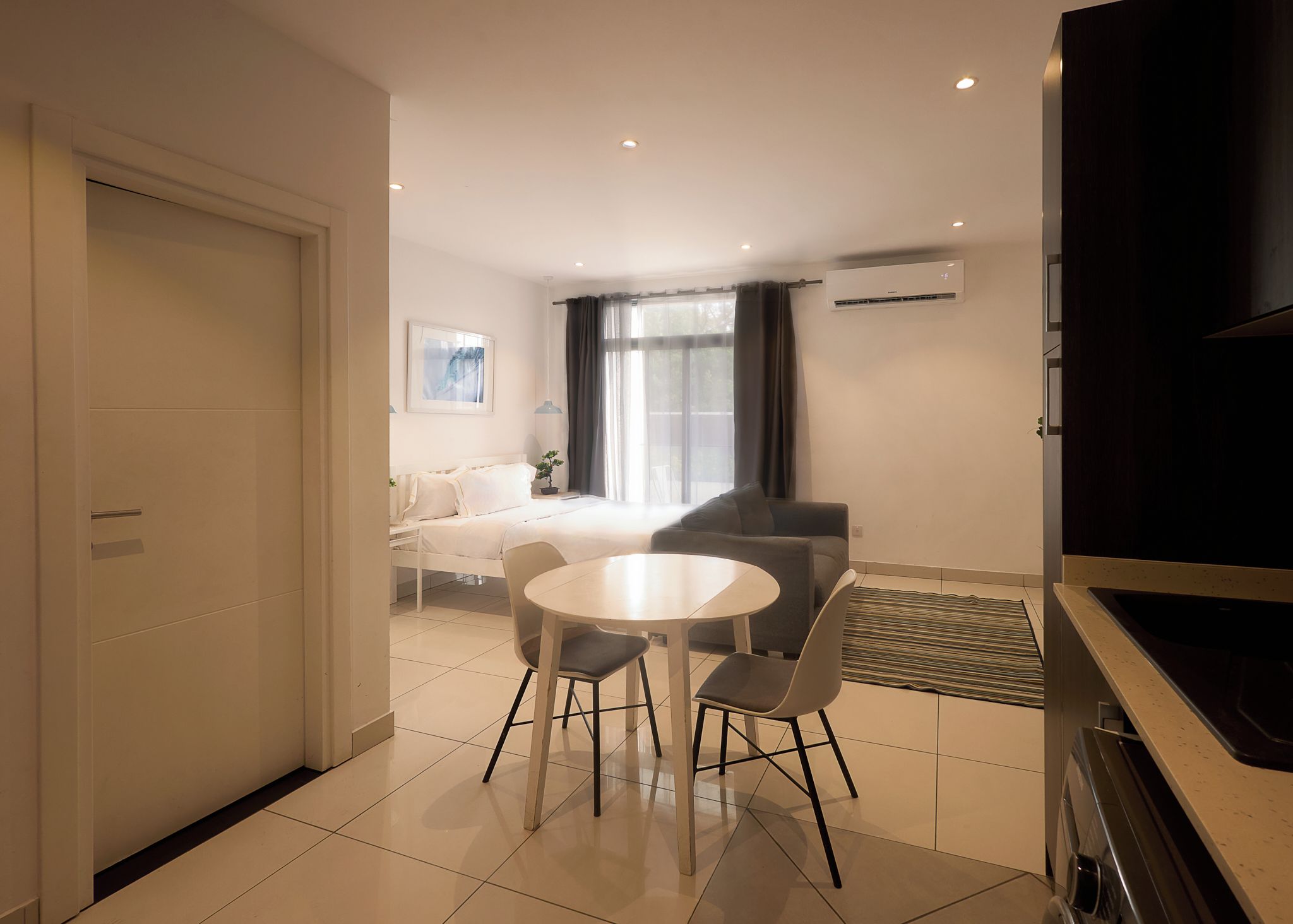Een moderne hotelkamer met een bed, een eettafel met stoelen, een televisie en een airconditioning.