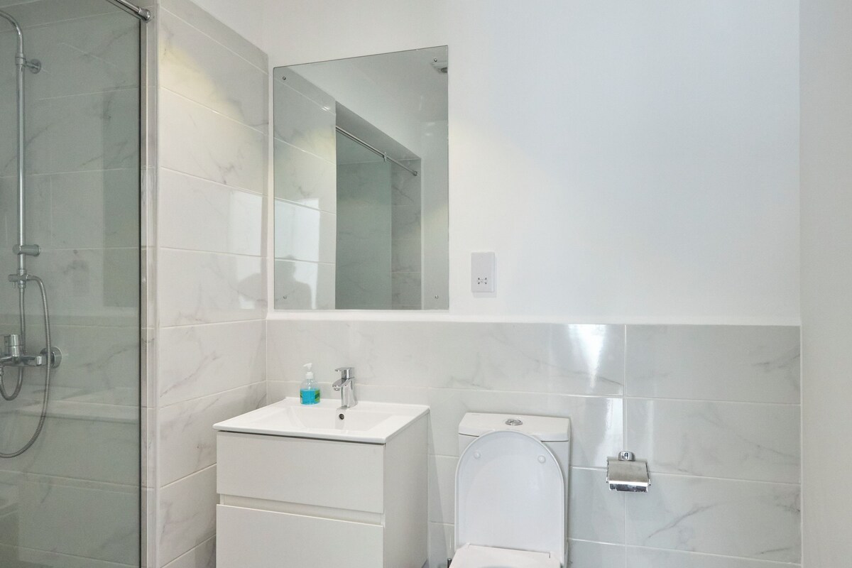 Ein modernes Badezimmer mit Duschkabine aus Glas, einem weißen Waschbecken, einer Toilette und einem Mülleimer.