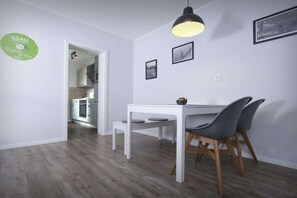 Ein Essbereich mit einem weißen Tisch und Stühlen, einer Pendelleuchte und gerahmten Bildern an der Wand.