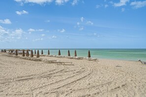 A beach with rows of sun loungers and umbrellas, a clear sky, and a calm sea. - Relax Poolside, Walk to Beach! Extended Naples Gem (Naples)