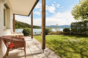 Eine Terrasse mit Blick auf einen See und Berge, ein Korbstuhl und ein Tisch.
