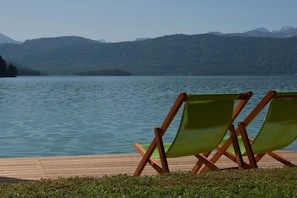 A wooden deck with two green chairs facing a calm lake with mountains in the background. - No. 1 - The Lake House (Walchensee)