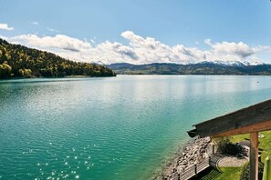 Une vue sur le lac, avec une terrasse en bois et un chemin de pierre menant à une zone herbeuse.