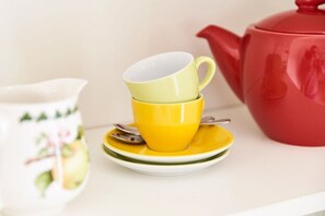 Une pile de tasses jaunes sur une assiette blanche, avec une théière rouge à côté.