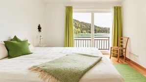 A bedroom with a bed, a chair, and a view of a lake through a balcony. - No. 1 - The Lake House (Walchensee)