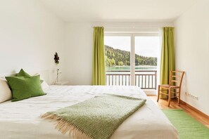 Ein Schlafzimmer mit Bett, Stuhl und Seeblick vom Balkon aus.