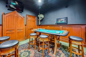 A room with a craps table, wooden bar stools, a television, and a decorative wall piece. - Ortonville Lakefront: Hot Tub & Casino Room (Ortonville)