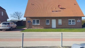 A single-story brick building with a tiled roof, a small front yard, and a parked car. - Holiday home with 3 bedrooms (Dornumersiel)